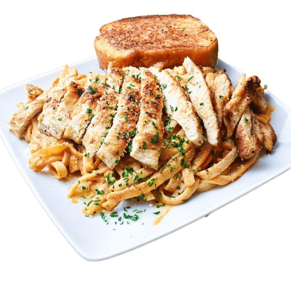 Grilled chicken fettuccine alfredo with parsley and a slice of garlic bread on a white plate.