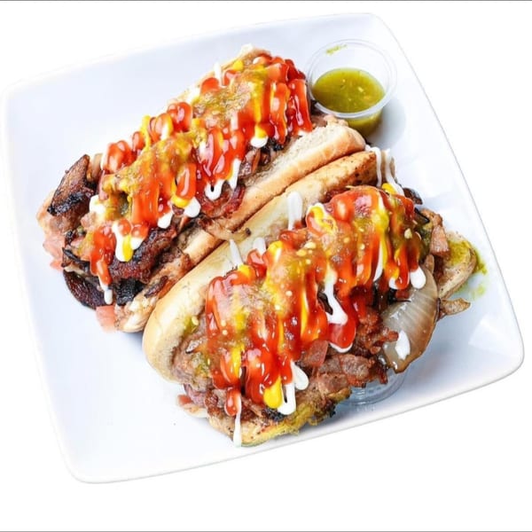 Two loaded hot dogs with various toppings and sauces, served on a white rectangular plate.